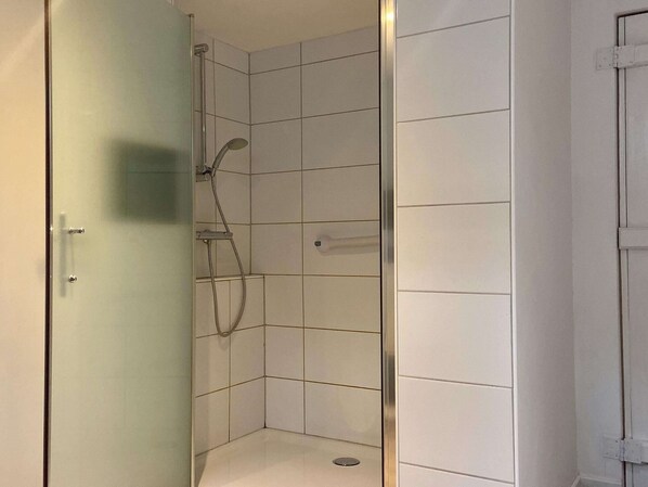 Piccola cabina doccia con piastrelle bianche e porta in vetro.