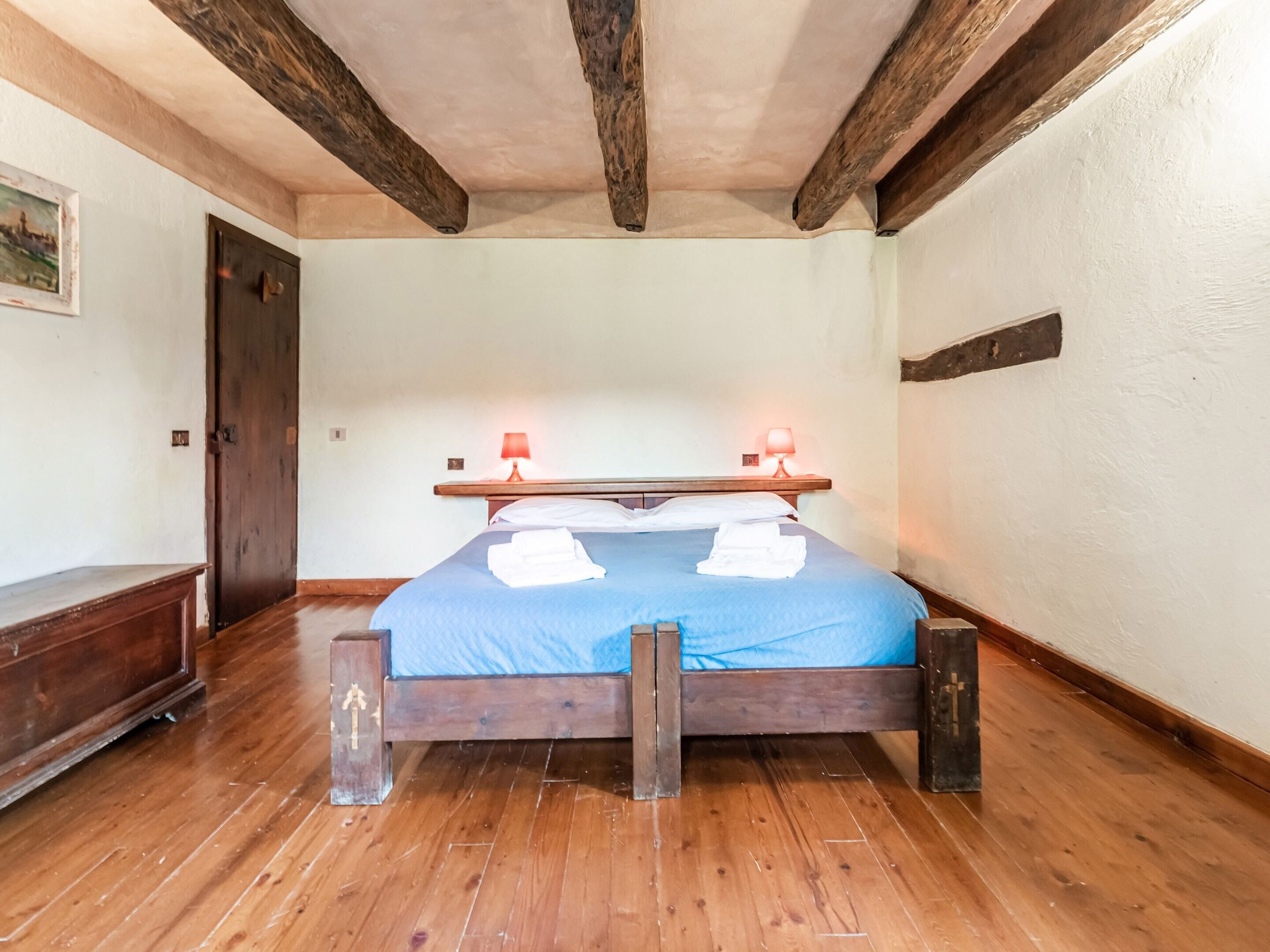 A bedroom with a wooden bed, two bedside lamps, a wooden bench, and a door.