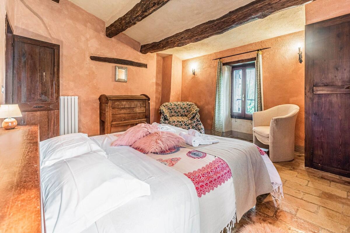 Un dormitorio con cama de madera, una silla, un radiador y una ventana con cortinas.
