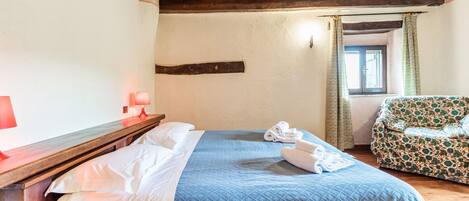 Un dormitorio con una cama de madera, una lámpara roja, un sofá estampado y un ventanal con cortinas.