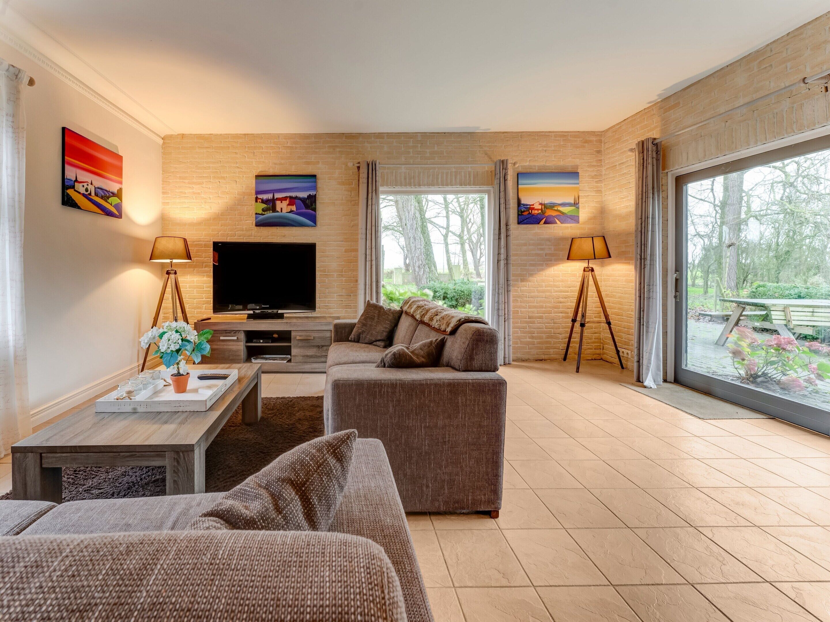 A modern living room with a flat-screen TV, two sofas, a coffee table, and a large window offering a view of the outdoors.