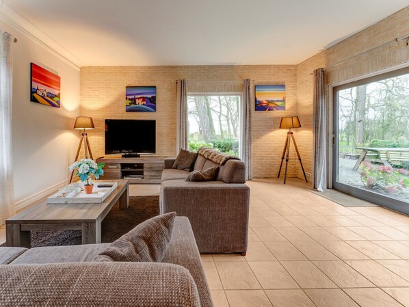 A modern living room with a flat-screen TV, two sofas, a coffee table, and a large window offering a view of the outdoors.