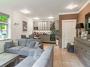 Ein modernes Wohnzimmer mit grauem Sofa, Essbereich, Küche mit grauen Schränken und einer Wand aus Ziegelsteinen.