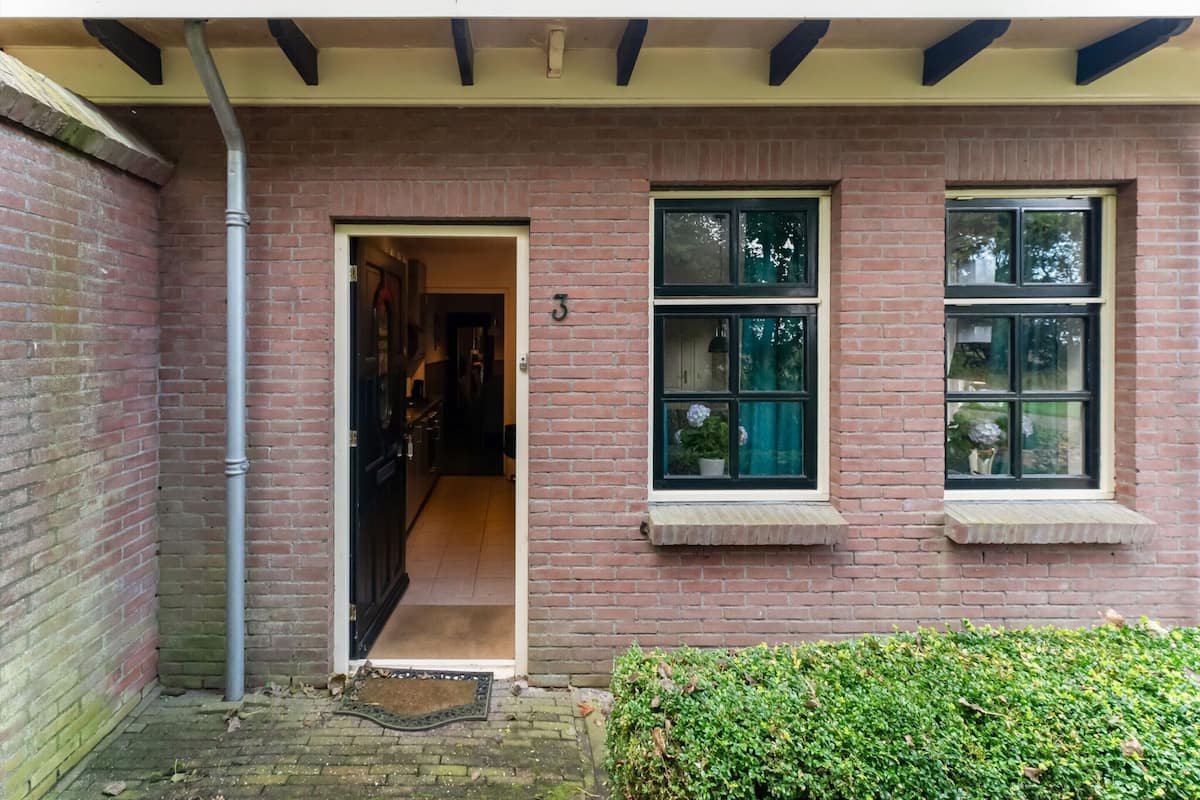 Ein Backsteinhaus mit einer Tür, die zu einem Flur führt, einem Fenster mit einem Blumentopf und einem kleinen Vordach über der Tür.