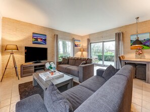 A modern living room with a flat-screen TV, a sofa, a coffee table, and a dining area with a table and chairs. - Cosy Apartment in Sint Maartensbrug Near the Beaches (Sint Maartensbrug)