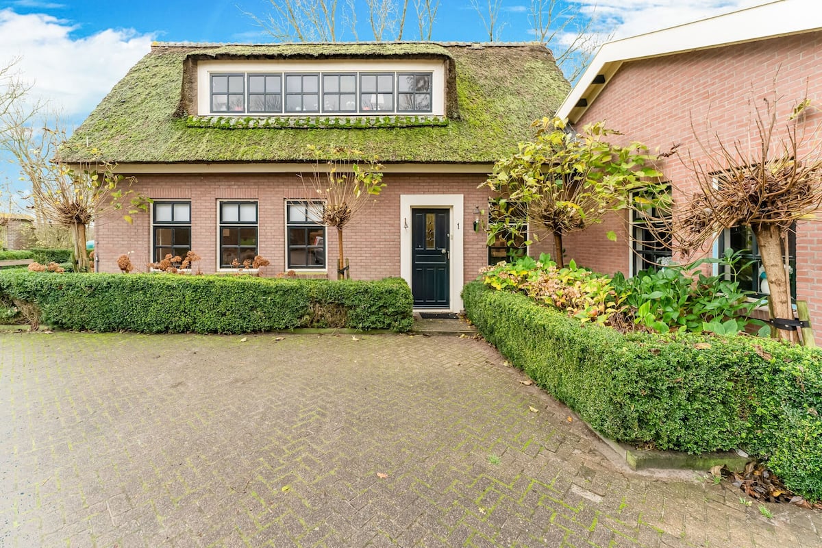 Ein Haus mit einem moosbewachsenen Dach, einer schwarzen Tür und einer Ziegel-Fassade.