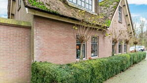 A traditional house with a thatched roof, brick walls, and a well-maintained hedge along the sidewalk.