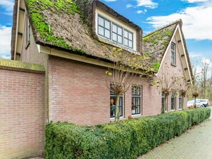 A two-story house with a thatched roof, brick walls, and a well-maintained hedge.