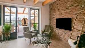 A modern living room with a large TV, comfortable seating, a zebra rug, and a brick wall. - Spacious Holiday Home Hazenborgh in Callantsoog Near Beach (Callantsoog)