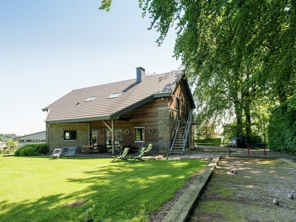 A rustic log cabin with a sloped roof, a porch with outdoor seating, and a ladder leading to the entrance.