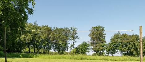 A grassy field with a volleyball net, trees, and a clear sky.