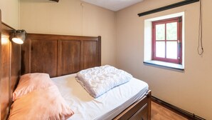 Un dormitorio con cama de madera, ventana con marco rojo y lámpara de pared.