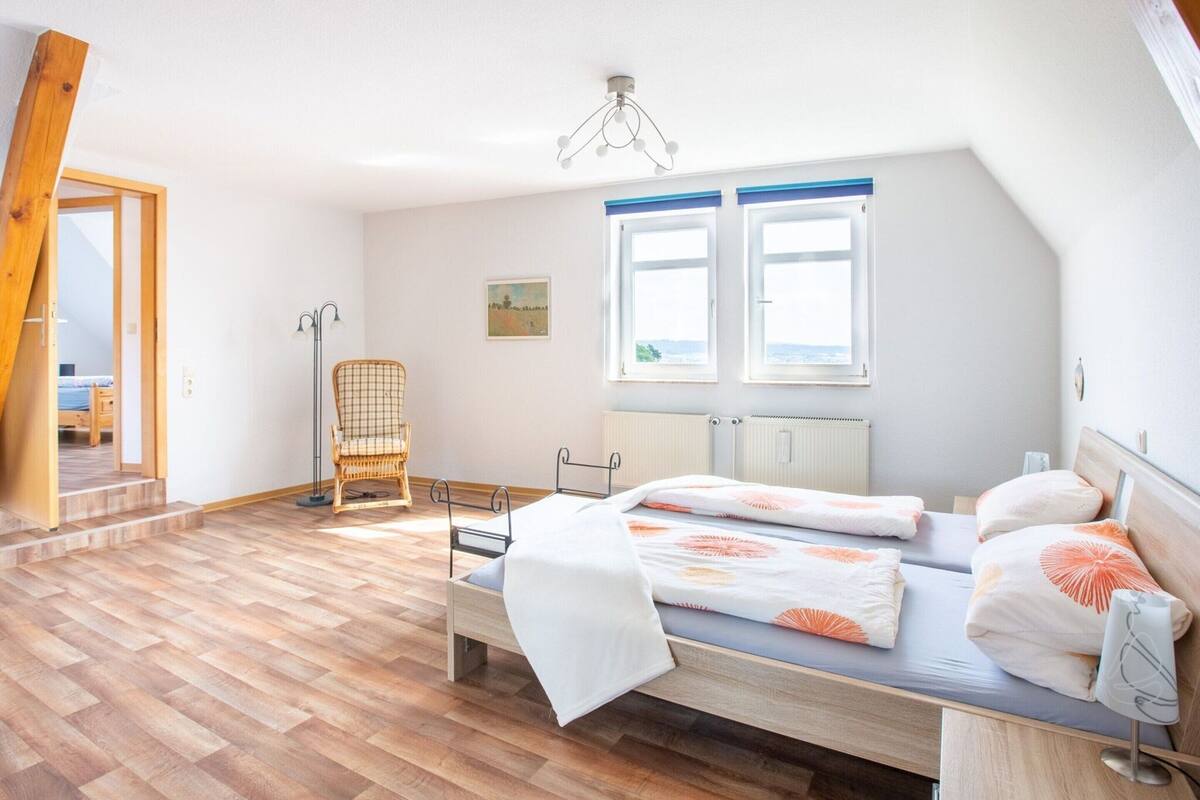 Quarto com cama, duas janelas, uma cadeira e um radiador.