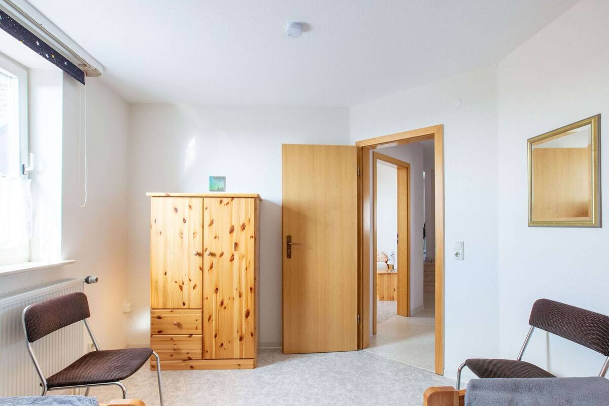 Quarto com armário de madeira, duas cadeiras, radiador e porta que dá para outro cômodo.