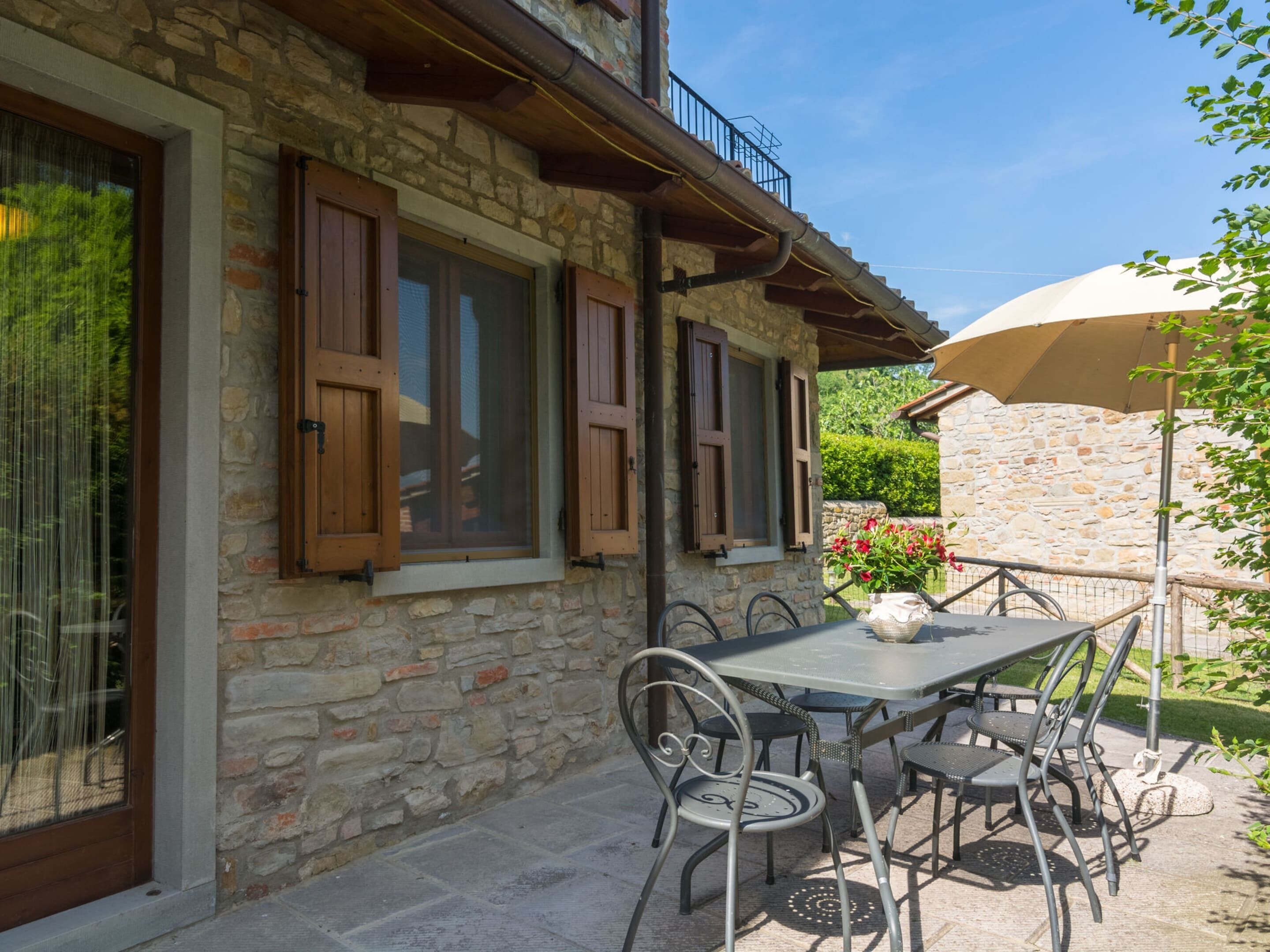 A stone building with a balcony, a table with chairs, and a large umbrella.