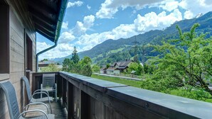 A wooden balcony with metal chairs, overlooking a mountainous landscape with houses and greenery. - Detached Modern Holiday Home With Sauna in the Salzburgerland (Bruck an der Grossglocknerstrasse)