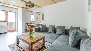 A spacious living room with a wooden ceiling, a gray sectional sofa, a wooden coffee table, and a dining area in the background. - Detached Modern Holiday Home With Sauna in the Salzburgerland (Bruck an der Grossglocknerstrasse)