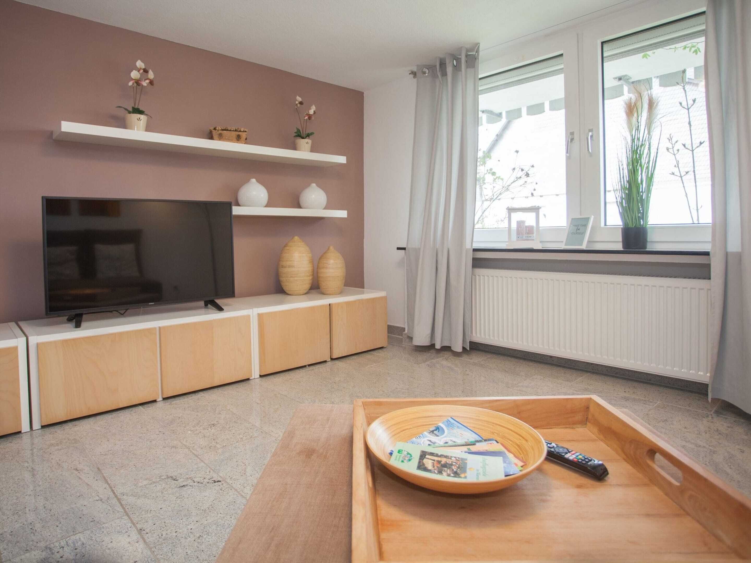 A modern living room with a flat-screen TV, wooden cabinets, and a tray with magazines and a remote control.
