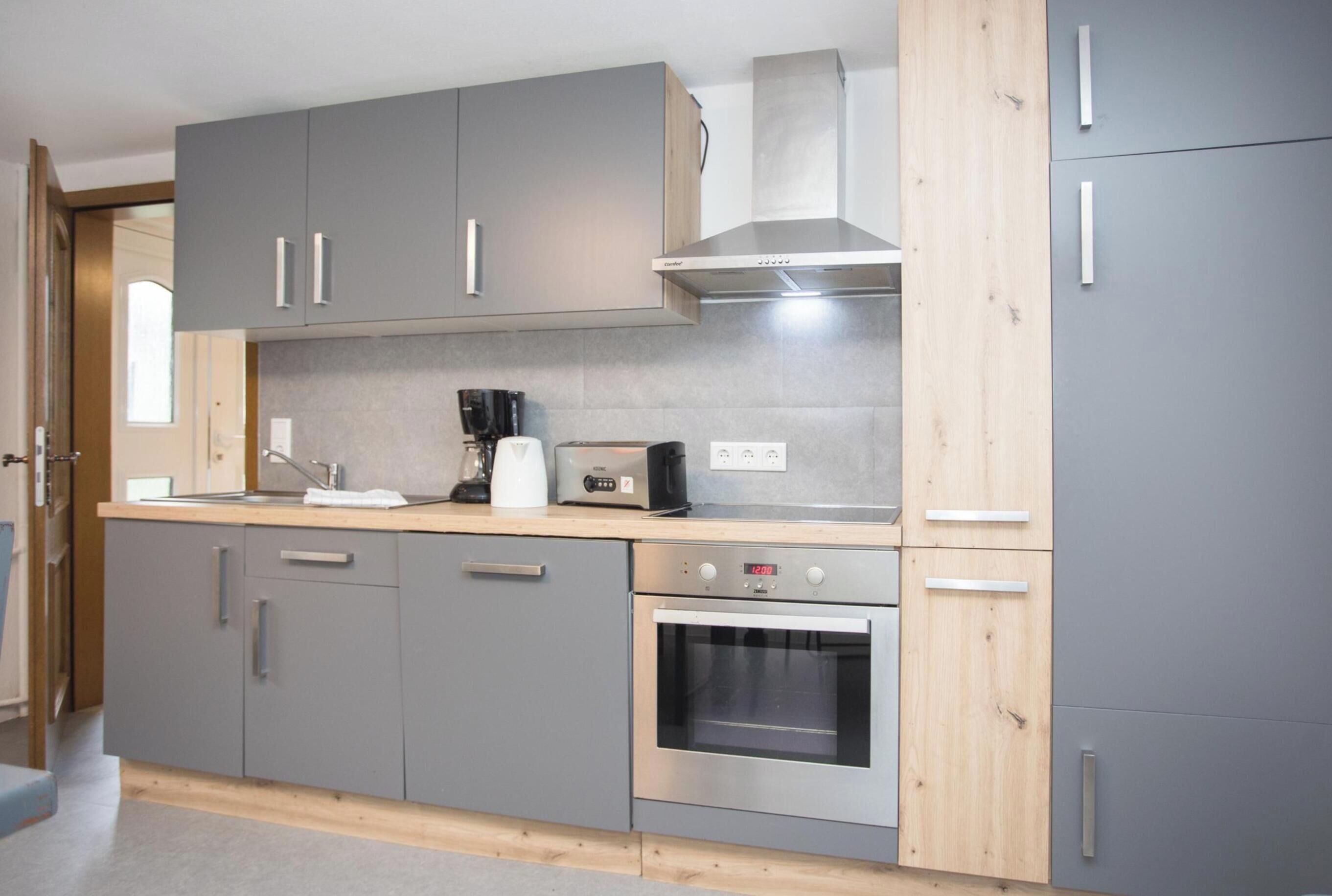 A modern kitchen with grey cabinets, a stainless steel oven, and a coffee maker.