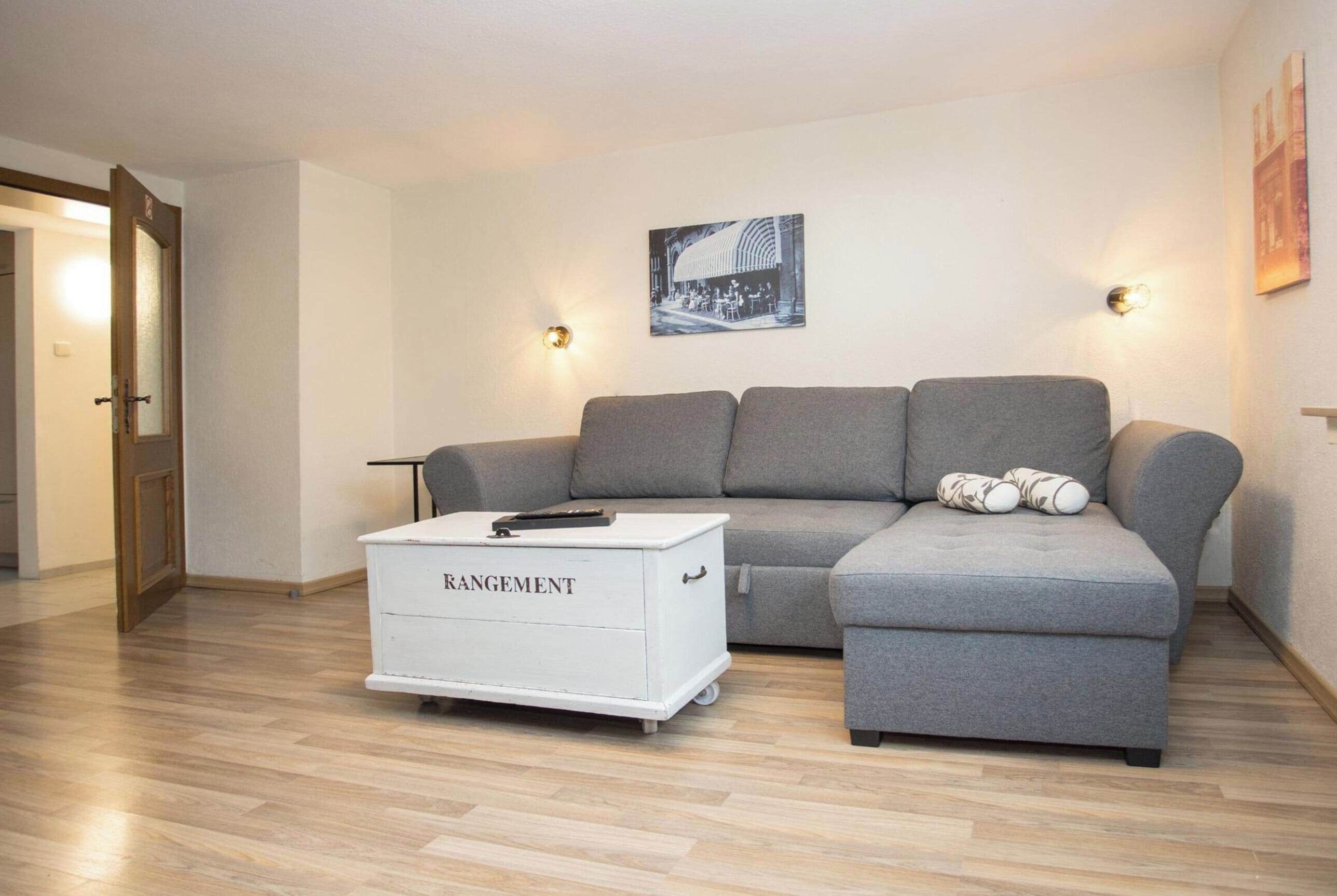 A living room with a grey sofa, a white storage unit labeled 'RANGEMENT,' and a black and white photograph on the wall.
