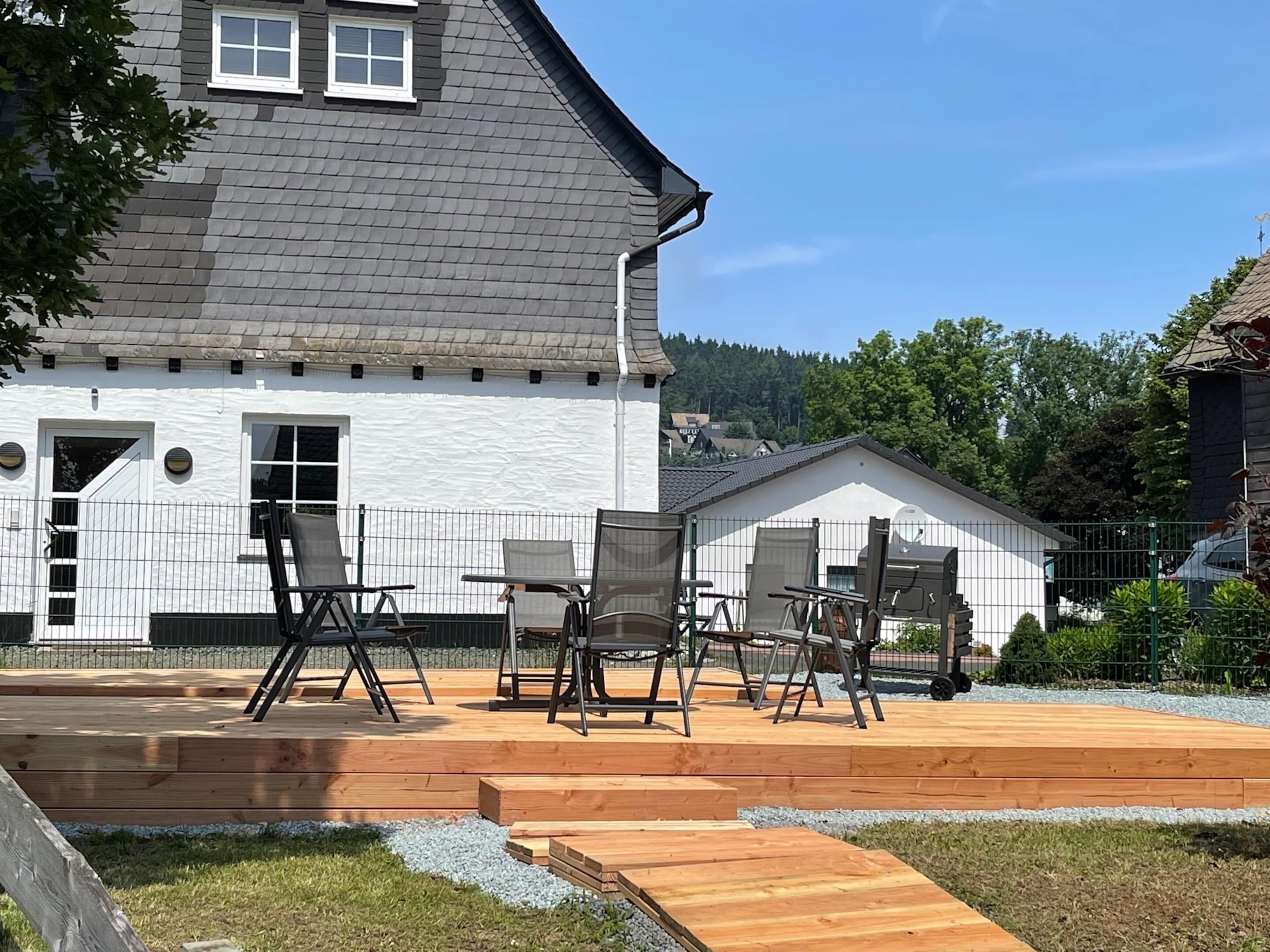 A house with a white exterior, a grey roof, and a wooden deck with outdoor furniture.