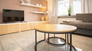 A modern living room with a round wooden table, a flat-screen TV, a sofa, and a window with curtains. - Large Apartment in Winterberg-neuastenberg Located Directly on a ski Area (Winterberg)