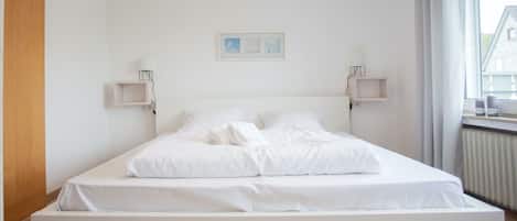 Une chambre à coucher au style minimaliste, avec un grand lit, deux tables de chevet, un tableau encadré au mur et une fenêtre avec des rideaux.