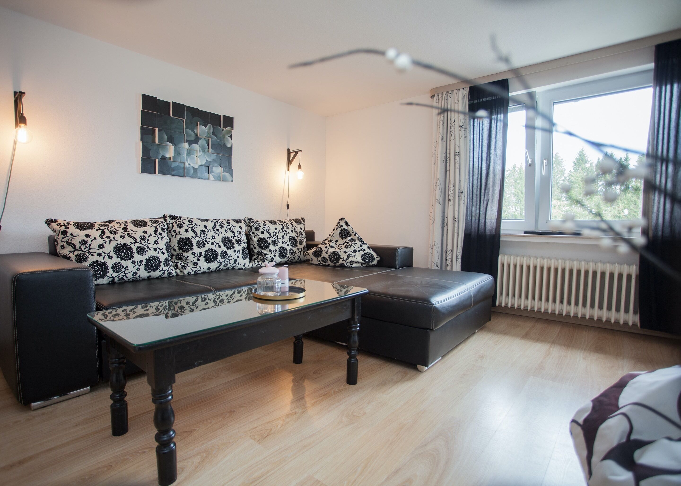 En moderne stue med sofasæt, et glasbord og udsigt til det fri gennem et vindue.
