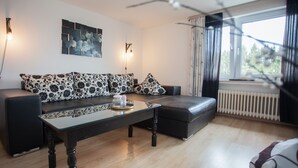 A modern living room with a sofa set, a glass coffee table, and a view of the outdoors through a window. - Modern Apartment in Neuastenberg Directly on a ski Area (Winterberg)