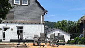 A house with a white exterior, a grey roof, and a wooden deck with outdoor furniture. - Modern Apartment in Neuastenberg Directly on a ski Area (Winterberg)