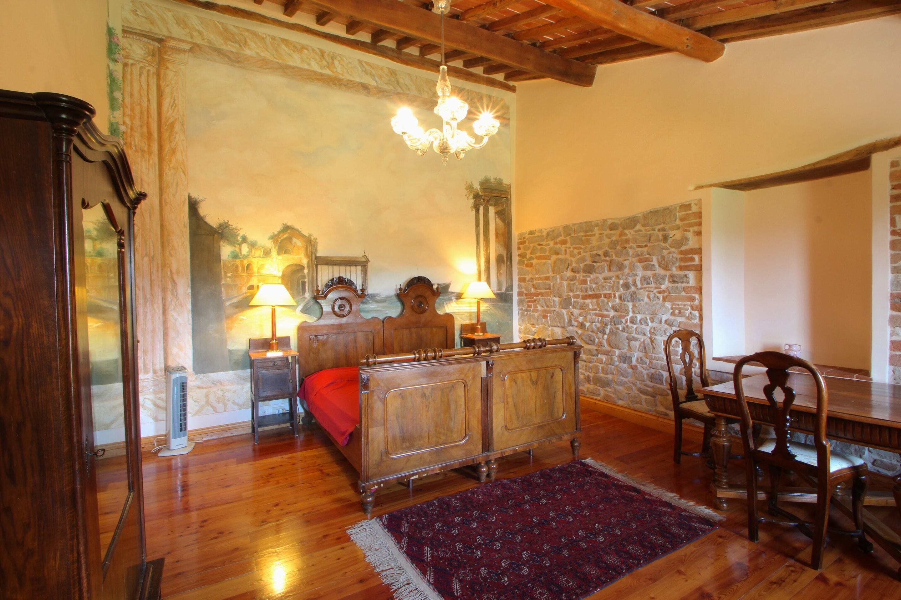 A bedroom with a bed, a dresser, a chair, a table, and a chandelier.