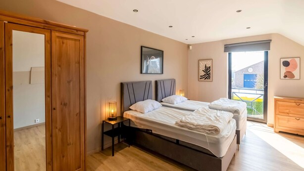 A bedroom with a large wardrobe, a bed with pillows, a bedside table with a lamp, and a window with a view.