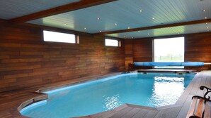 A large indoor swimming pool with wooden walls and ceiling, benches along the edge, and large windows.