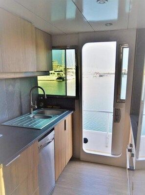 A compact kitchen with a sink, a window overlooking a marina, and a door leading to an outdoor area. - Luxury Yacht in La Rochelle With a Terrace (La Rochelle)