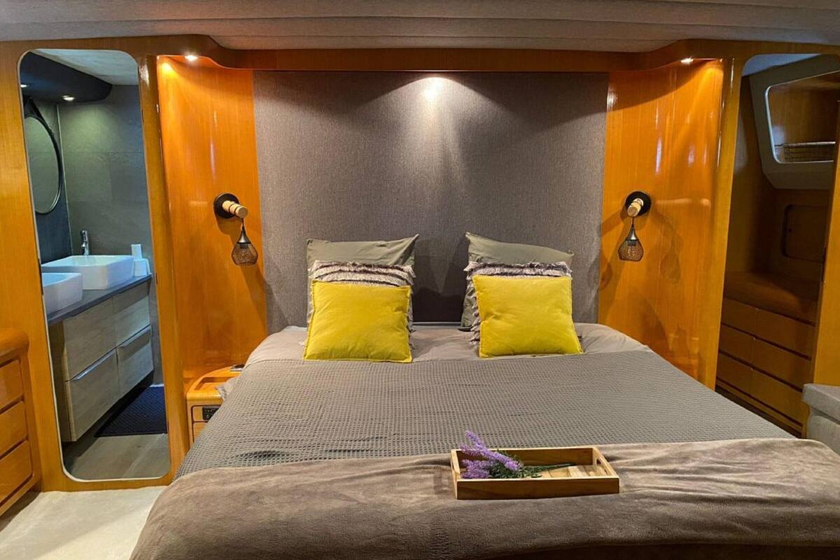 A compact bedroom with a bed, two pillows, a bedside table, and a small wooden tray with flowers.