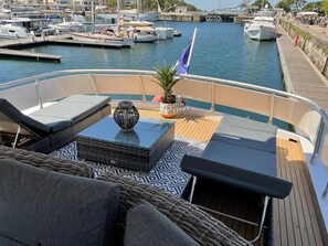 Cubierta de barco con sillones de descanso, una mesa y una planta en maceta.