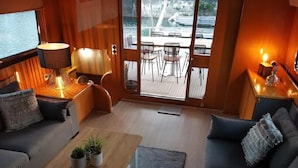 A cozy interior with a sofa, a wooden coffee table with plants, and a view of an outdoor deck with chairs and a table. - Luxury Yacht in La Rochelle With a Terrace (La Rochelle)