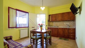Une petite cuisine avec des meubles en bois, une table à manger avec des chaises, un canapé et un téléviseur fixé au mur.