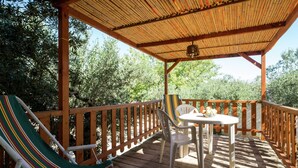 Une terrasse en bois surmontée d’un toit en bambou, avec deux chaises et une table où sont disposés des fruits.