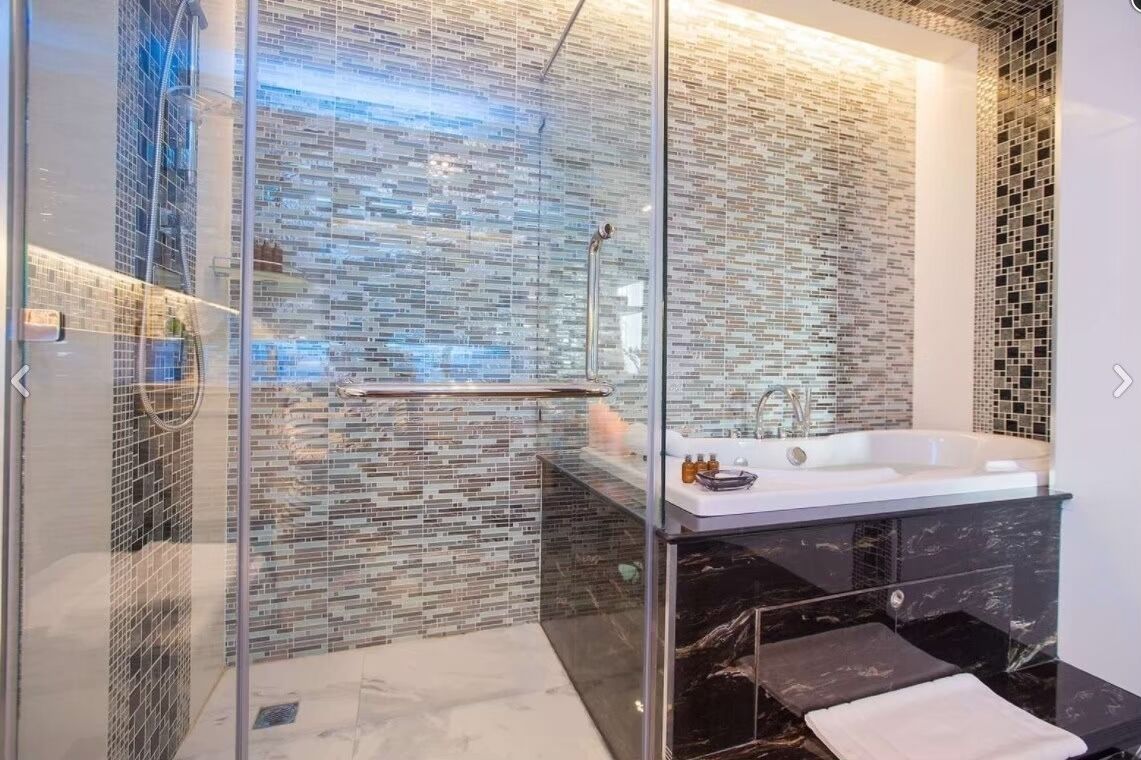 A modern bathroom with a glass-enclosed shower, a large bathtub, and a mosaic-tiled wall.