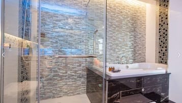 A modern bathroom with a glass-enclosed shower, a large bathtub, and a mosaic-tiled wall.