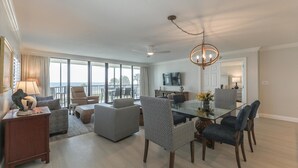 Un salon spacieux avec une table à manger en verre, des sièges confortables, un grand téléviseur et un balcon avec vue.
