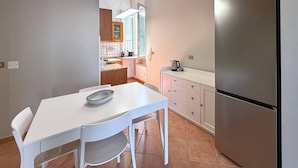 Une cuisine moderne avec une table blanche, un réfrigérateur en acier inoxydable et une fenêtre équipée de stores.