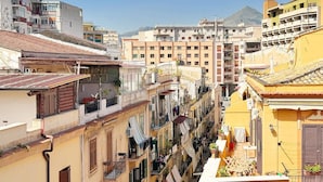 Une rue étroite bordée d’immeubles à plusieurs étages, de balcons où est étendu du linge, et une montagne en arrière-plan.