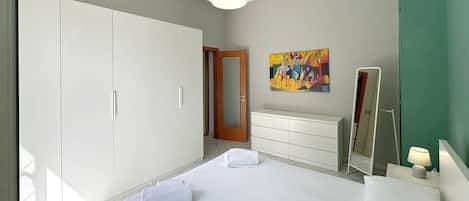 Een moderne slaapkamer met een groot bed, een kledingkast, een dressoir, een spiegel en een schilderij aan de muur.