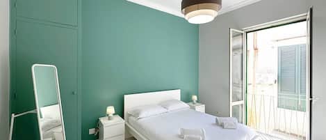 A modern bedroom with a bed, bedside tables, a mirror, and a view through a glass door.