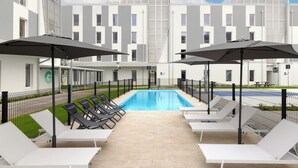 Un espace piscine doté de chaises longues et de parasols, entouré d’un bâtiment moderne comportant de nombreux balcons.