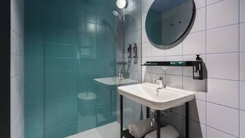 Un baño moderno con cabina de ducha de vidrio, un lavabo blanco y un espejo redondo.