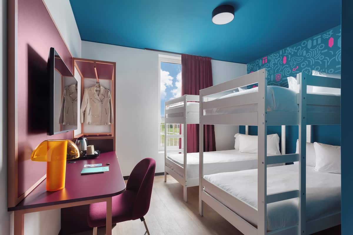 A room with bunk beds, a desk with a chair, a mirror, and a window with curtains.