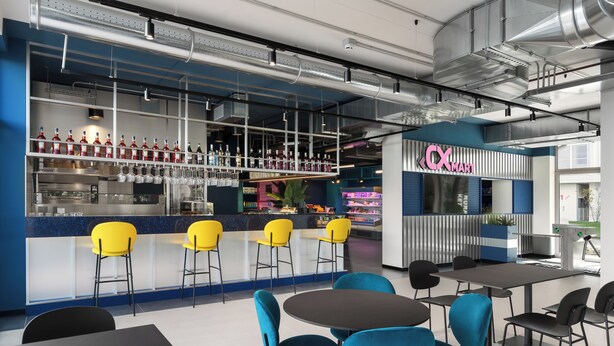 Un espace bar moderne aux couleurs bleu et blanc, avec un comptoir bien garni de bouteilles et de verres, ainsi que plusieurs chaises jaunes et bleues disposées autour de tables.